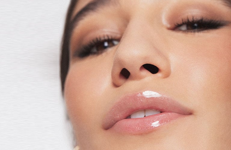 Foto con fondo blanco. En el centro, se observa la parte inferior del rostro de una mujer. Sus labios están cerrados y en evidencia, con piel en tonos naturales.